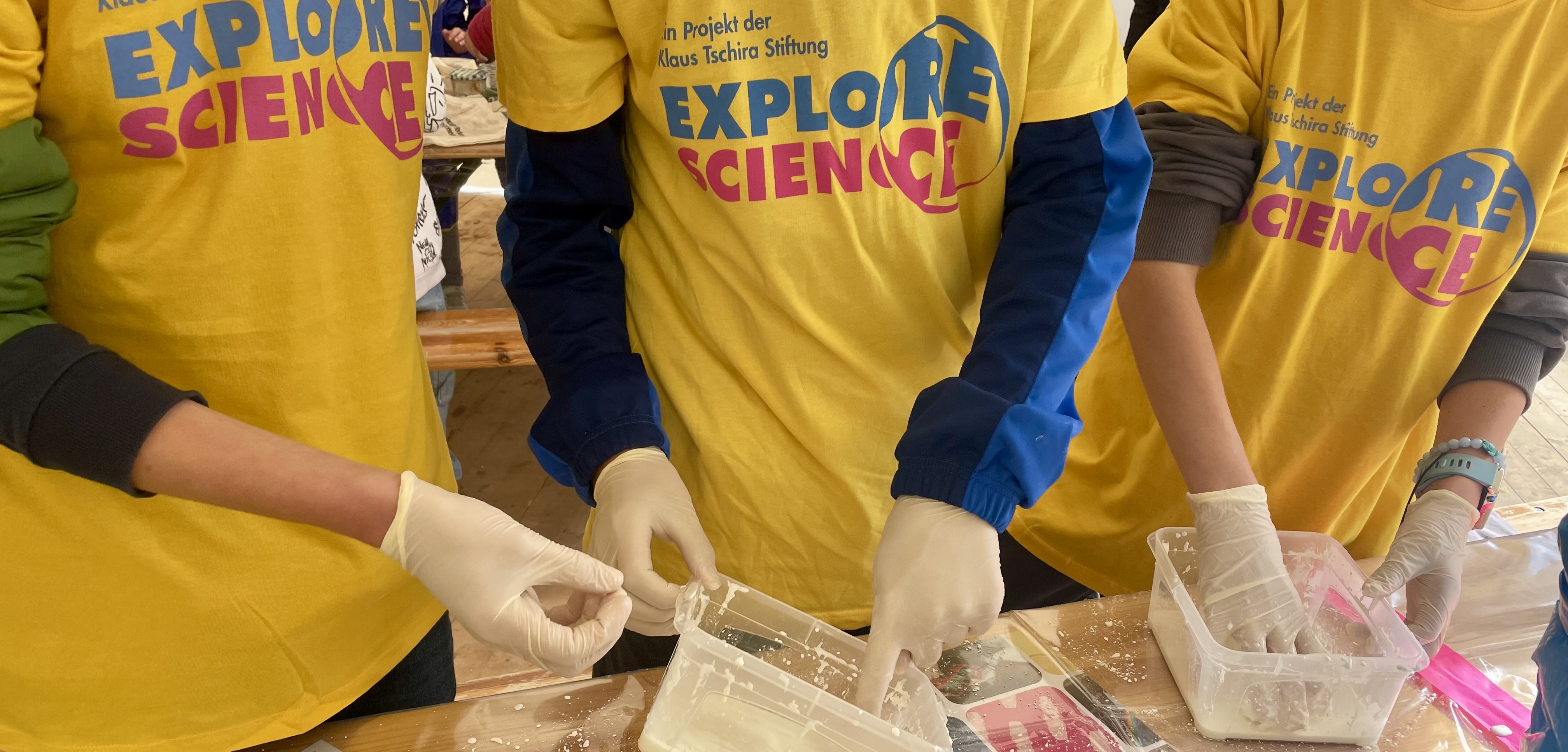 Three children wearing ‘Explore Science’ T-shirts experiment with non-Newtonian fluid.